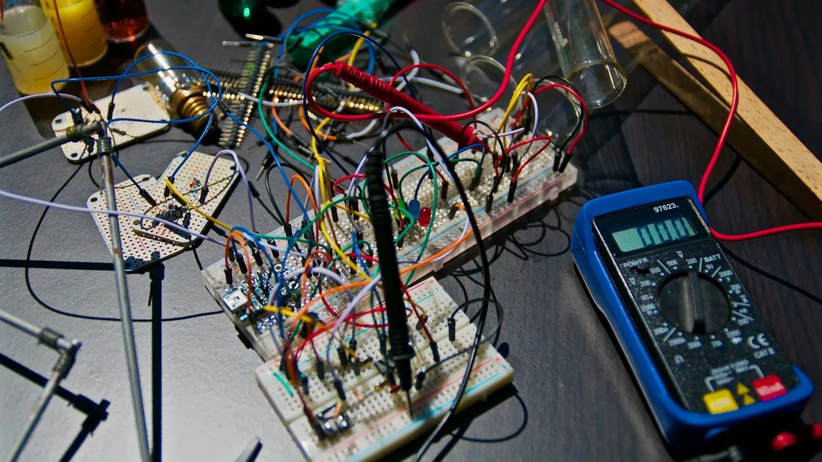 An electronics prototype on breadboards, wired to a multimeter on a workbench.